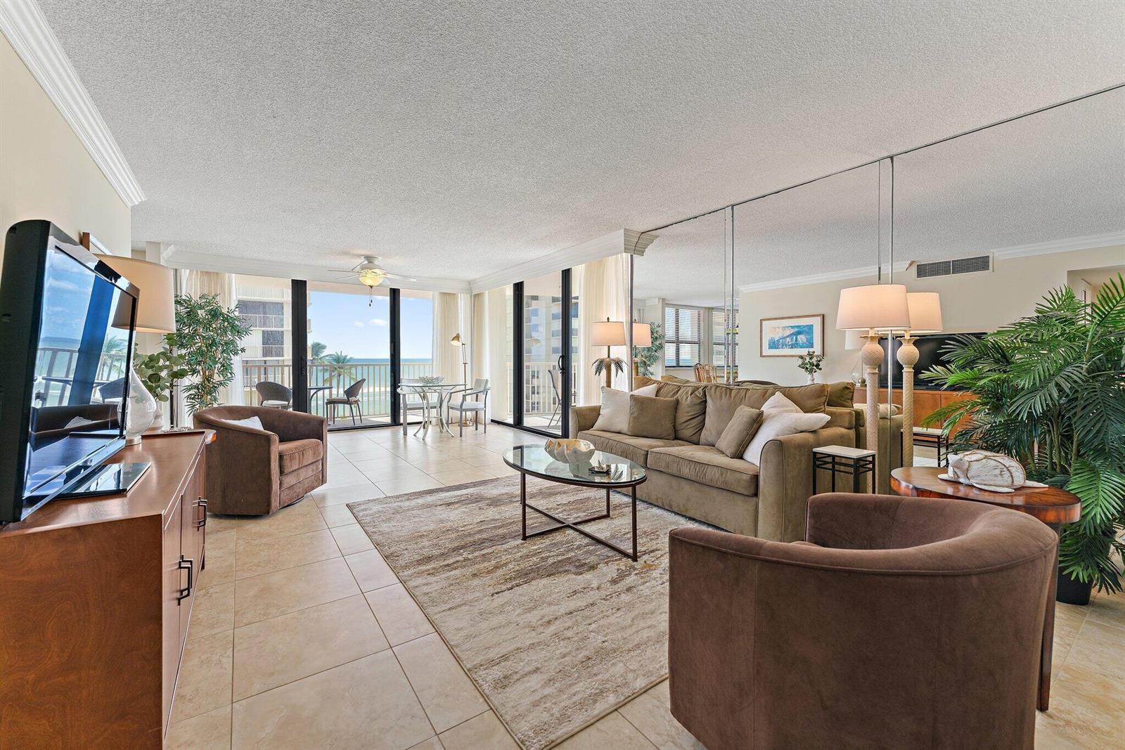 A living room features a beige sofa, two brown armchairs, tile floors, and mirrored walls — 5480 N Ocean Drive, Singer Island FL 33404, SINGER ISLAND, FL