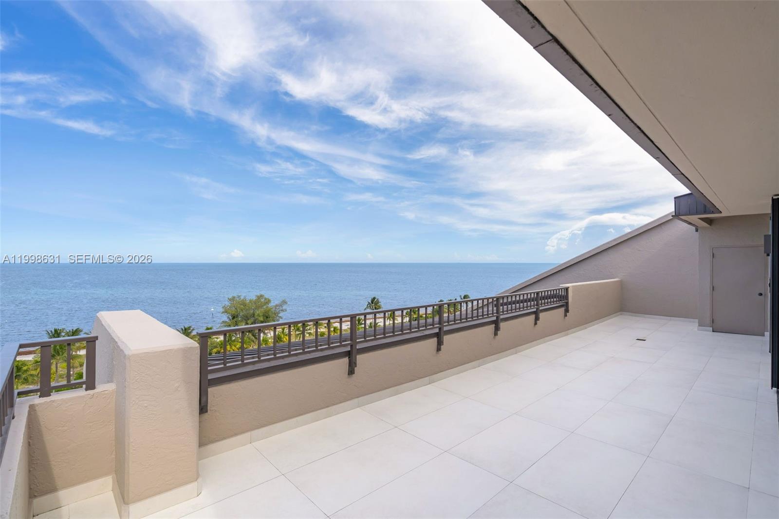 A spacious, tiled balcony overlooks the ocean with a metal railing and a beige wall — 251 Crandon Blvd # 1037, Key Biscayne FL 33149, KEY BISCAYNE, FL
