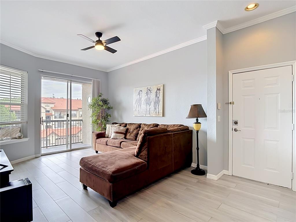 A living room features a brown sectional sofa, a ceiling fan, and a sliding glass door — 18107 PEREGRINES PERCH PLACE UNIT 6304, LUTZ, FL