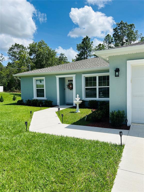 A light green house exterior features a white front door, walkway, and small fountain — 8848 N PARADISEA DRIVE, CITRUS SPRINGS, FL
