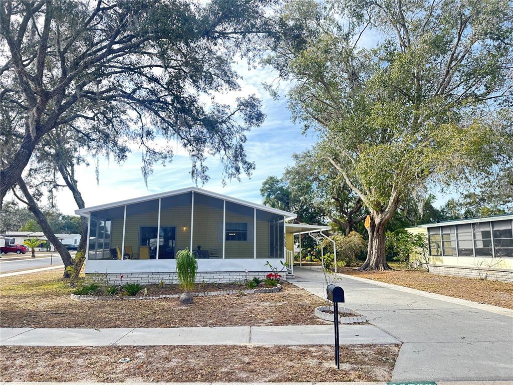 A yellow manufactured home features a large screened-in front porch and a concrete driveway — 16735 OLIVAUD STREET, HUDSON, FL