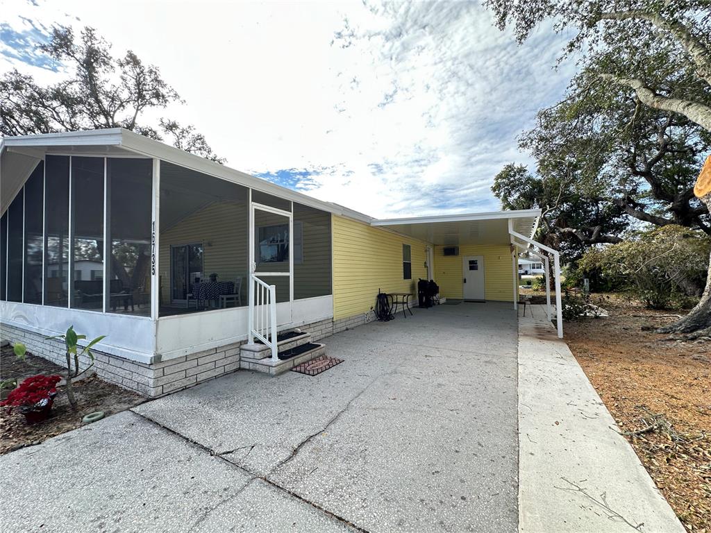 A yellow mobile home features a screened-in porch, a concrete driveway, and a covered carport — 16735 OLIVAUD STREET, HUDSON, FL