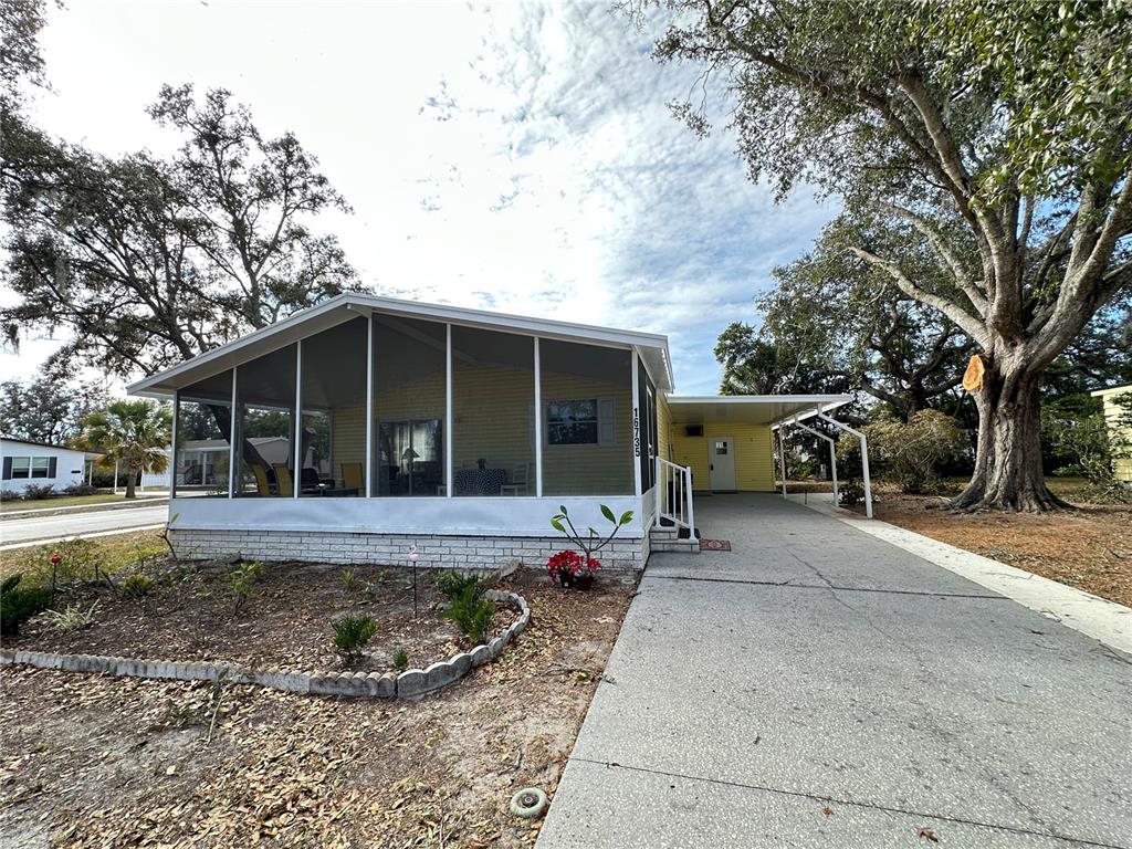 A yellow mobile home features a large screened-in porch and an attached carport — 16735 OLIVAUD STREET, HUDSON, FL