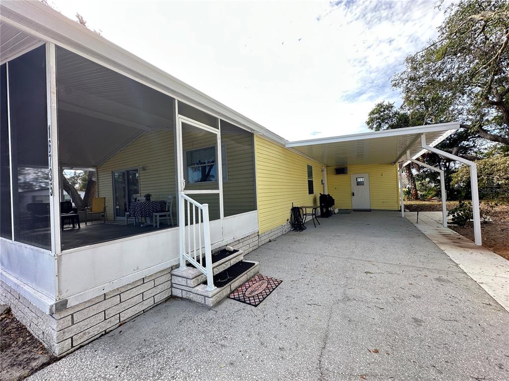 A yellow mobile home features a screened-in porch, a concrete driveway, and a metal carport — 16735 OLIVAUD STREET, HUDSON, FL