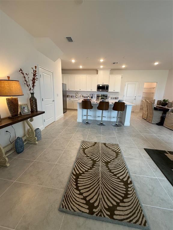 An open-concept kitchen features white cabinetry, a central island with bar seating, and tile flooring — 4870 PRAIRIE PRESERVE RUN NW, ST CLOUD, FL