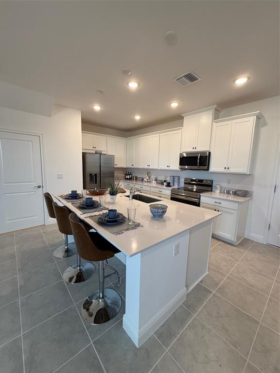 A kitchen features white cabinets, a quartz-topped island with bar seating, and gray tile flooring — 4870 PRAIRIE PRESERVE RUN NW, ST CLOUD, FL
