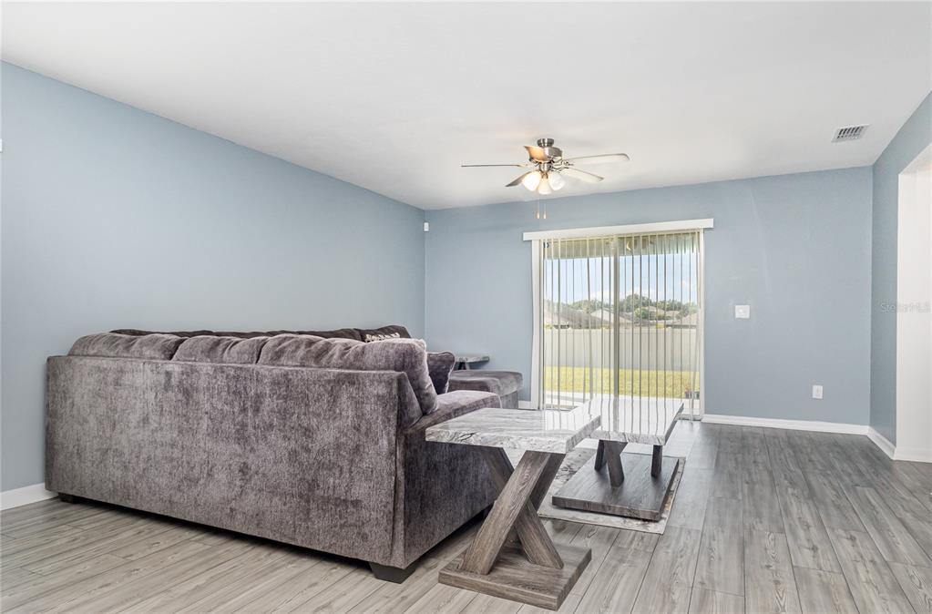 A living room features light blue walls, gray wood-look flooring, a sectional sofa, and sliding doors — 1760 CANAAN LOOP, DUNDEE, FL
