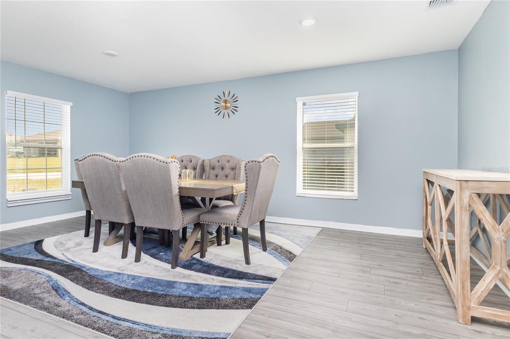 A dining room features gray walls, wood-look flooring, a patterned area rug, and upholstered chairs — 1760 CANAAN LOOP, DUNDEE, FL