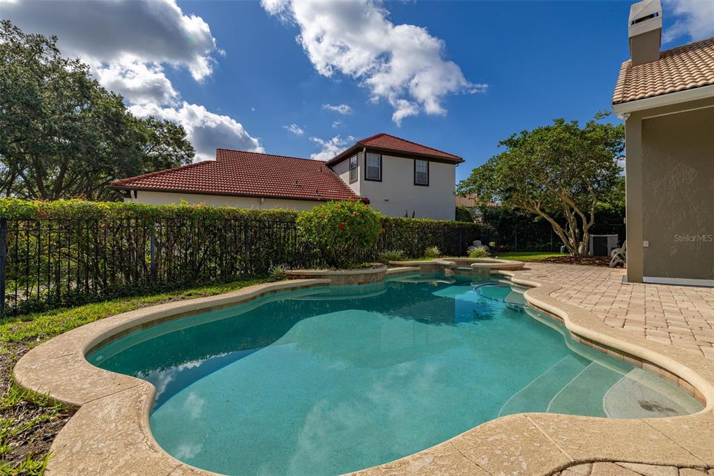 A backyard swimming pool with a stone deck sits beside a house with a tiled roof — 1855 VISTA ROYALE BOULEVARD, ORLANDO, FL
