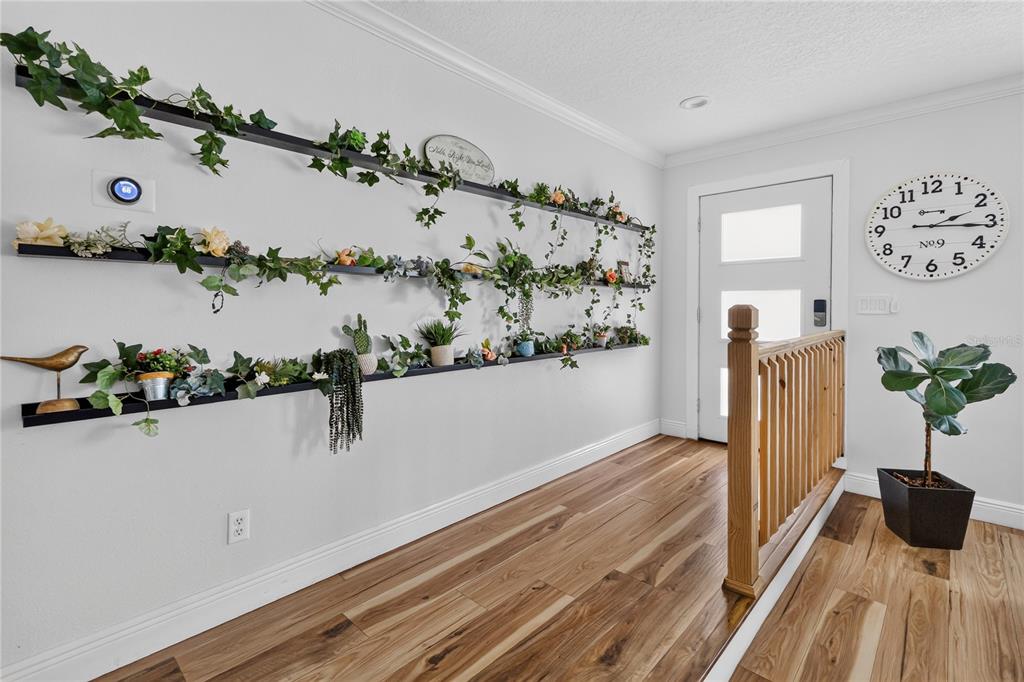A hallway features three long shelves decorated with artificial plants and a wooden stair railing — 5316 HALYARD COURT, WINTER PARK, FL