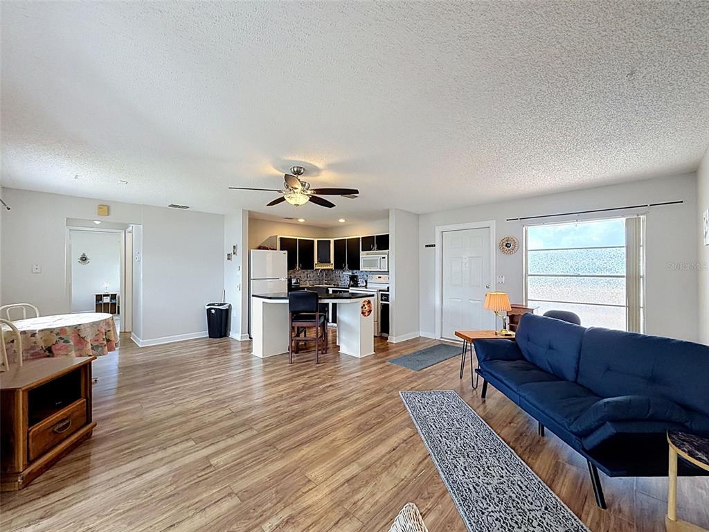 An open-concept living room and kitchen feature wood-look flooring, a ceiling fan, and a sofa — 12024 BAYONET LANE UNIT 9GB, NEW PORT RICHEY, FL