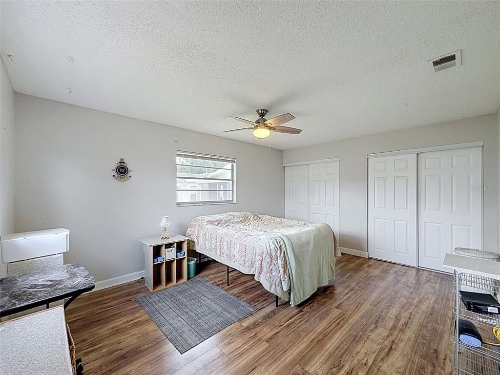 A bedroom features wood-look flooring, a ceiling fan, a bed, and two white closet doors — 12024 BAYONET LANE UNIT 9GB, NEW PORT RICHEY, FL