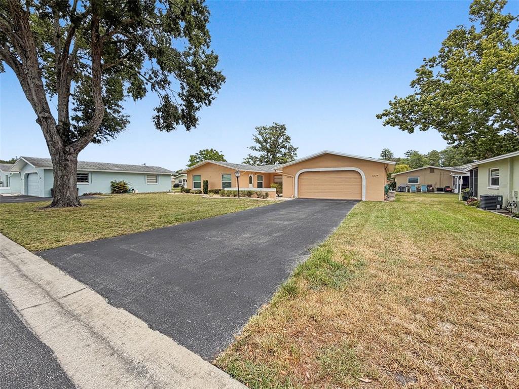 A tan single-story house with a two-car garage and a paved driveway sits on grass — 12024 BAYONET LANE UNIT 9GB, NEW PORT RICHEY, FL