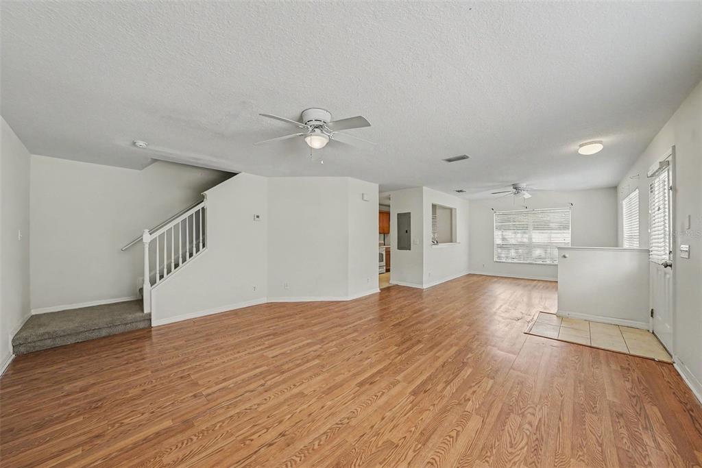 An open-concept living area features light wood flooring, white walls, and a staircase — 217 PENMARK STONE PLACE, VALRICO, FL