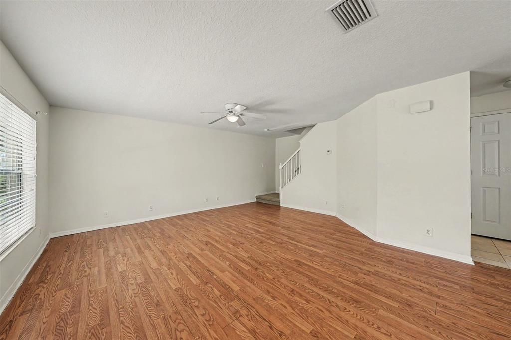 An empty living room features wood-look flooring, white walls, a ceiling fan, and a staircase — 217 PENMARK STONE PLACE, VALRICO, FL