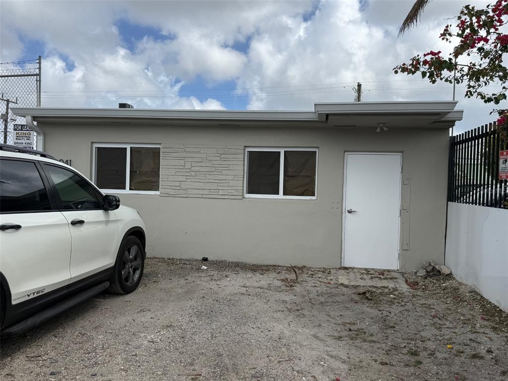 A single-story commercial building exterior with a white door, two windows, and a gravel lot — 14041 NW 20TH AVENUE, OPA LOCKA, FL