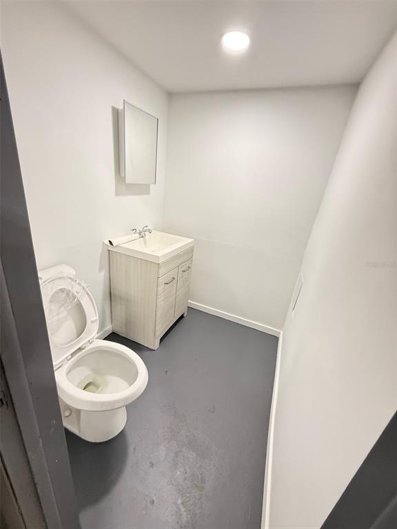A small bathroom features a white toilet, a light wood vanity, and gray flooring — 14041 NW 20TH AVENUE, OPA LOCKA, FL