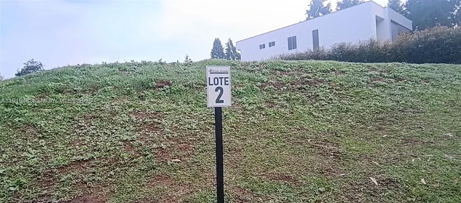 A sign labeled Lote 2 stands on a grassy, sloped plot of land — Vereda Mampuesto Sector Garrido #2, C Colombia, C