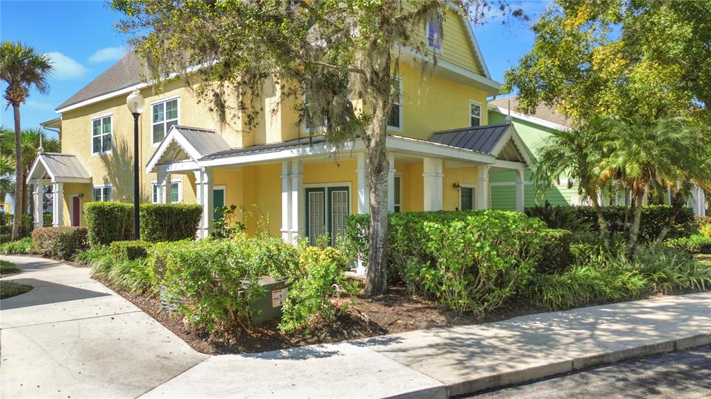A yellow two-story building with a covered porch and surrounding landscaping on a sunny day — 3002 BONFIRE BEACH DRIVE UNIT 102, KISSIMMEE, FL
