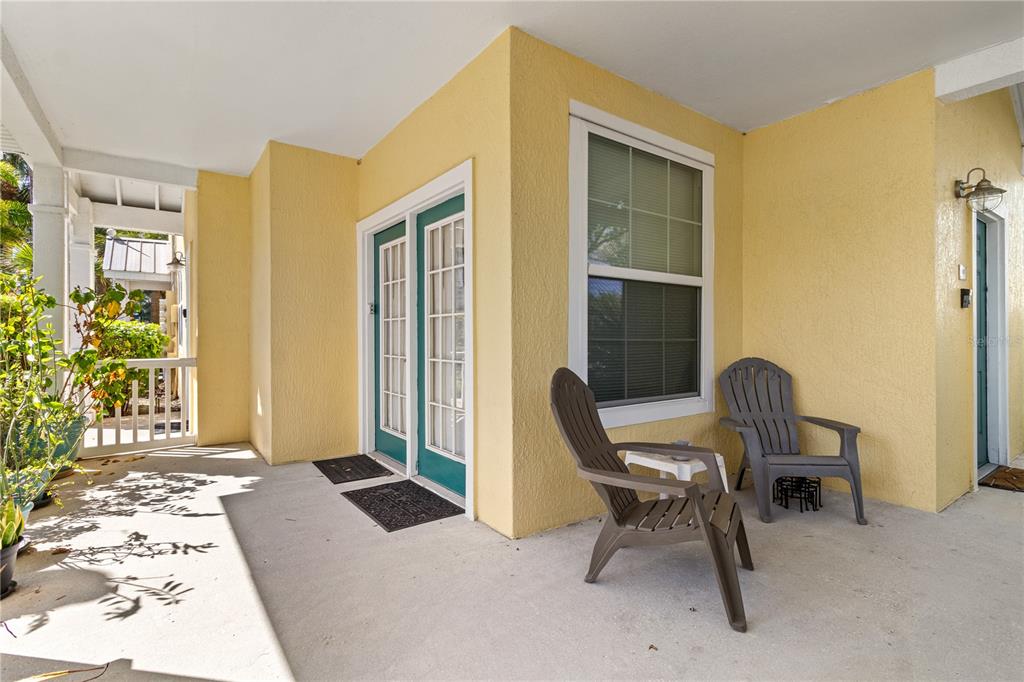 A covered porch with yellow walls, two gray chairs, and a set of glass doors — 3002 BONFIRE BEACH DRIVE UNIT 102, KISSIMMEE, FL