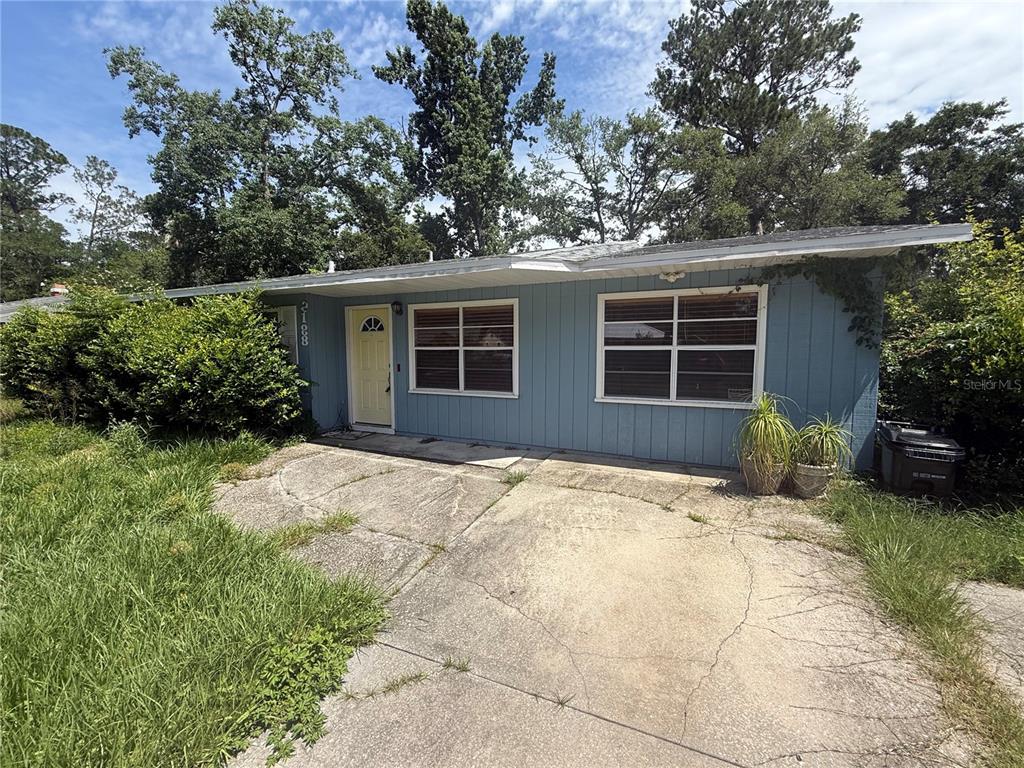 A single-story blue house with a concrete driveway and overgrown lawn under a cloudy sky — 2188 NW 42ND AVENUE, GAINESVILLE, FL