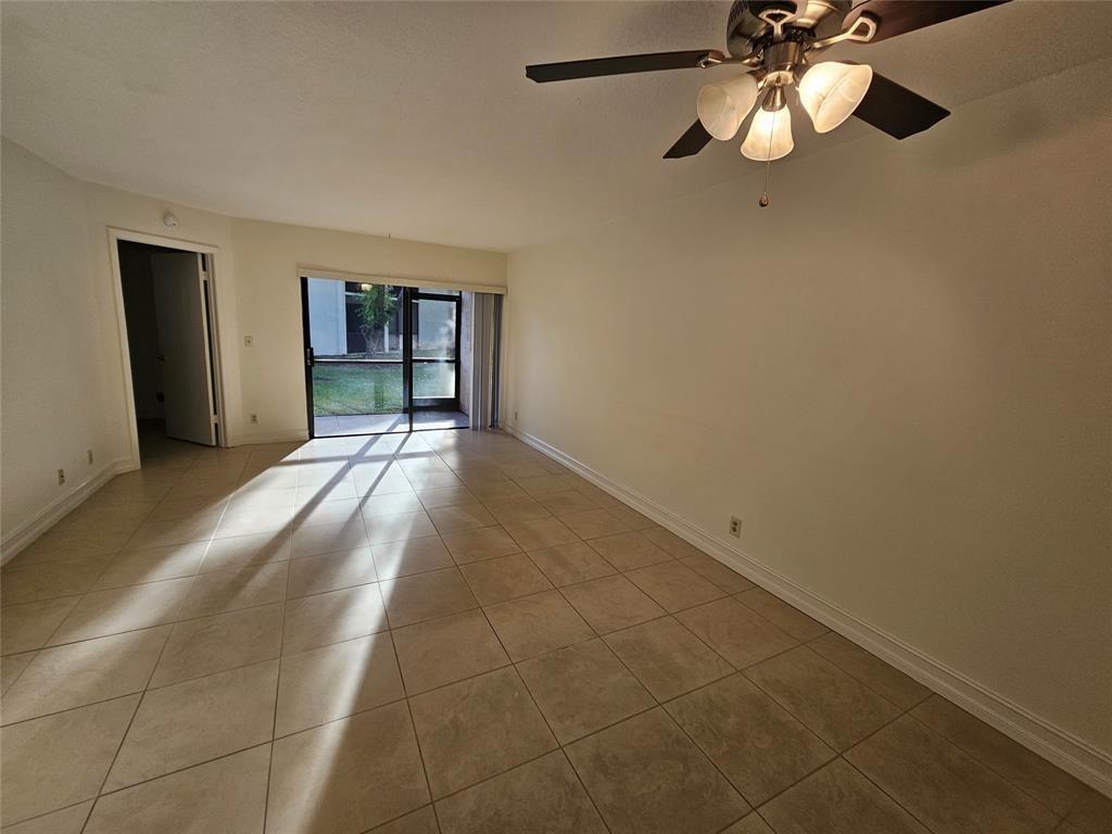 An empty living room features beige tile flooring, a ceiling fan, and a sliding glass door — 5583 Courtyard Drive # 5583, Margate FL 33063, MARGATE, FL