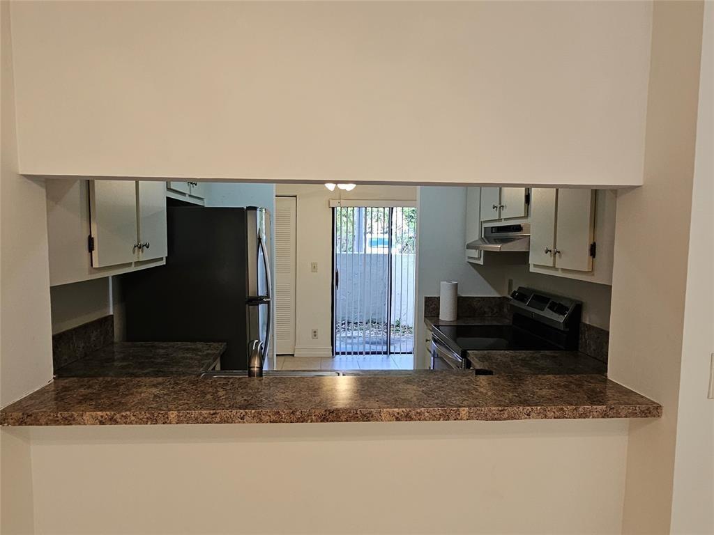 A kitchen pass-through window overlooks a kitchen with dark countertops and white cabinets — 5583 Courtyard Drive # 5583, Margate FL 33063, MARGATE, FL
