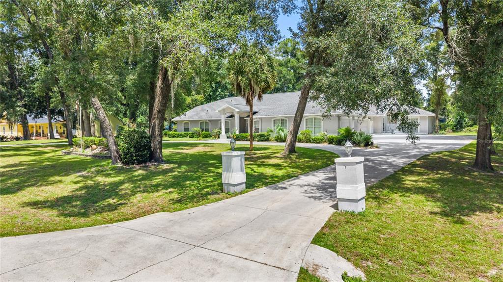 A concrete driveway leads to a single-story house surrounded by trees and a grassy lawn — 11108 NW 70TH CIRCLE, CHIEFLAND, FL