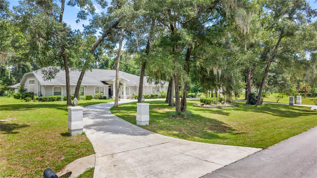 A single-story house with a concrete driveway sits on a grassy lot with large trees — 11108 NW 70TH CIRCLE, CHIEFLAND, FL