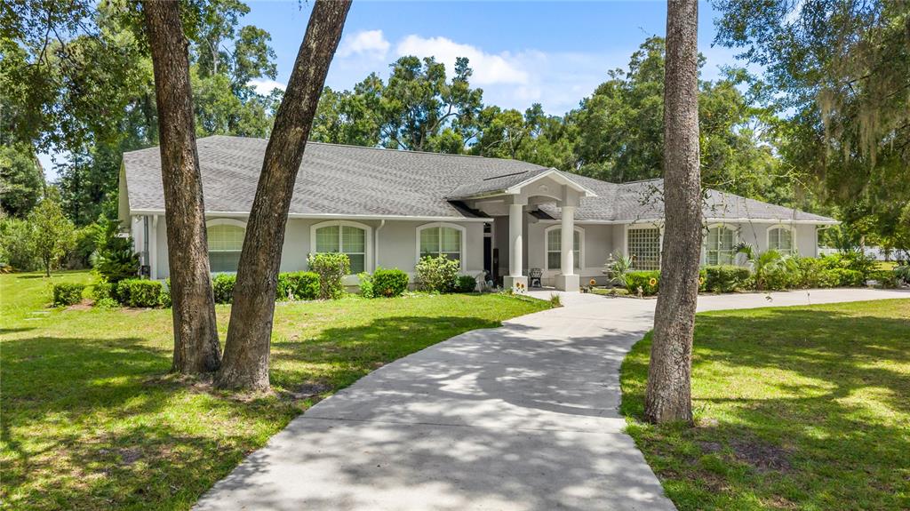 A single-story house with a gray roof, white exterior, and a concrete driveway among trees — 11108 NW 70TH CIRCLE, CHIEFLAND, FL