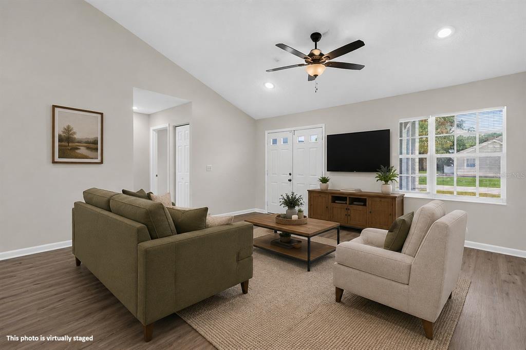 This virtually staged living room features light walls, wood-look flooring, a vaulted ceiling, and furniture — 22 PINELYNN LANE, PALM COAST, FL