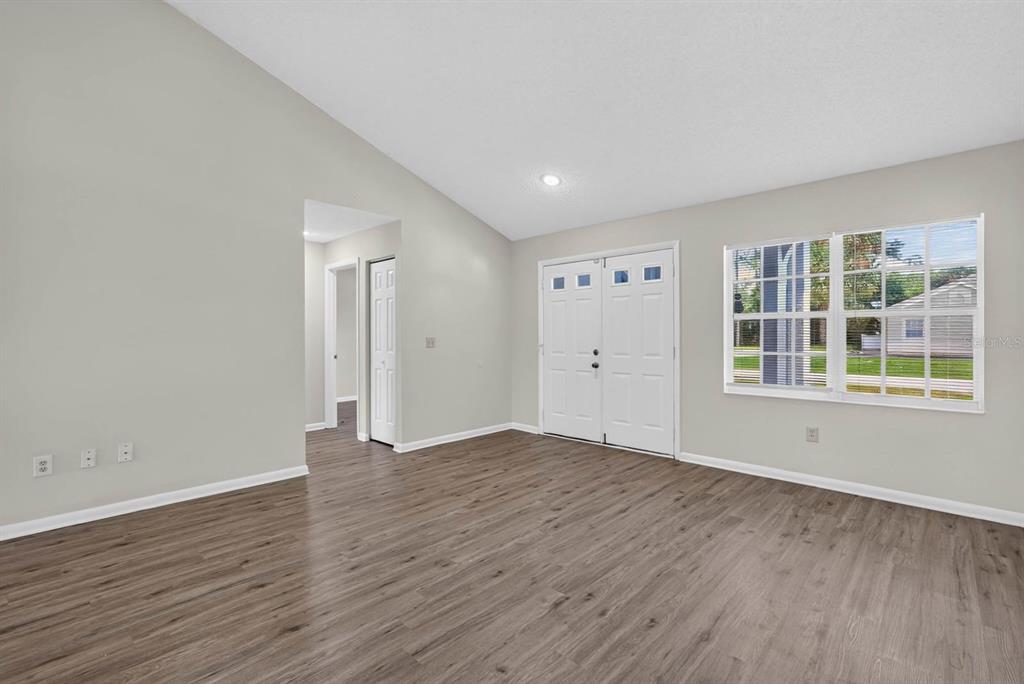 A bright living room features wood-look flooring, light gray walls, a double-door entrance, and windows — 22 PINELYNN LANE, PALM COAST, FL