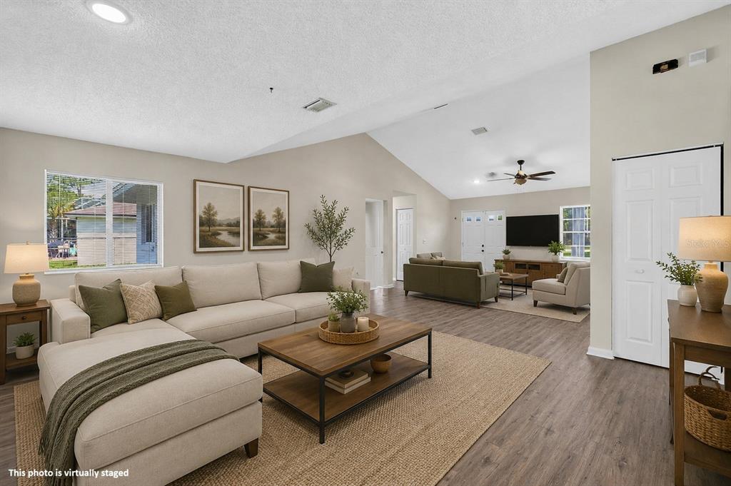 This virtually staged living room features vaulted ceilings, wood-look flooring, and a large sectional sofa — 22 PINELYNN LANE, PALM COAST, FL