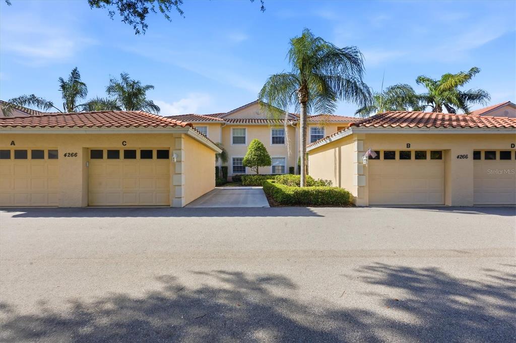A view of a residential building exterior featuring four garage doors and a palm tree — 4266 VICENZA DRIVE UNIT A39, VENICE, FL