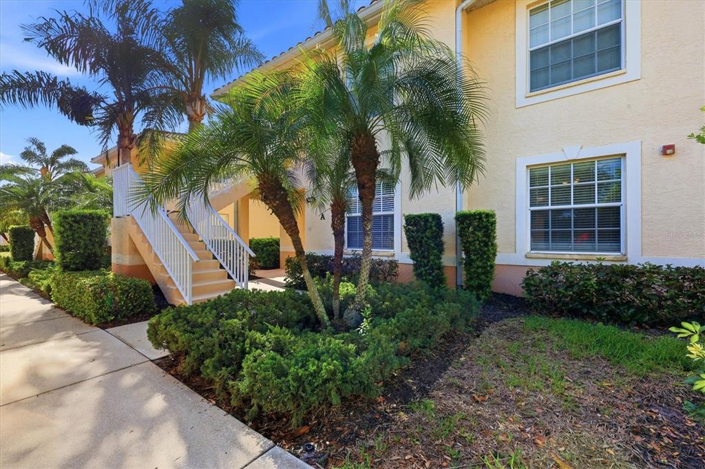 A two-story apartment building exterior features a white staircase, palm trees, and manicured landscaping — 4266 VICENZA DRIVE UNIT A39, VENICE, FL
