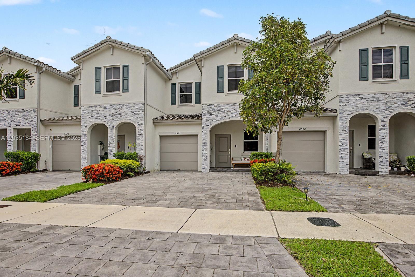 A row of three two-story townhouses with stone-accented facades, paved driveways, and attached garages — 2644 SE 13th St, Homestead FL 33035, HOMESTEAD, FL