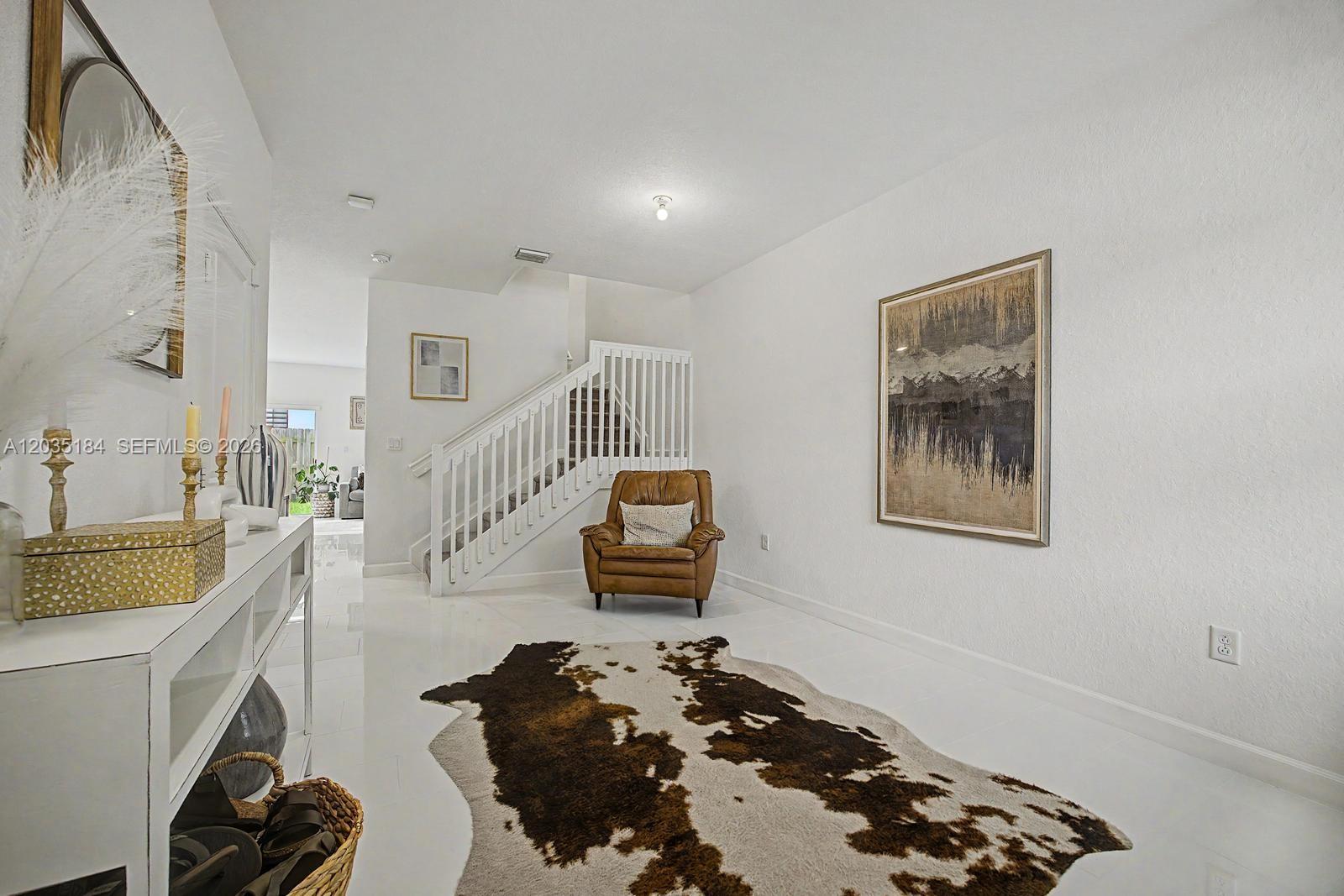 A white-tiled entryway features a brown leather armchair, a cowhide rug, and a staircase — 2644 SE 13th St, Homestead FL 33035, HOMESTEAD, FL