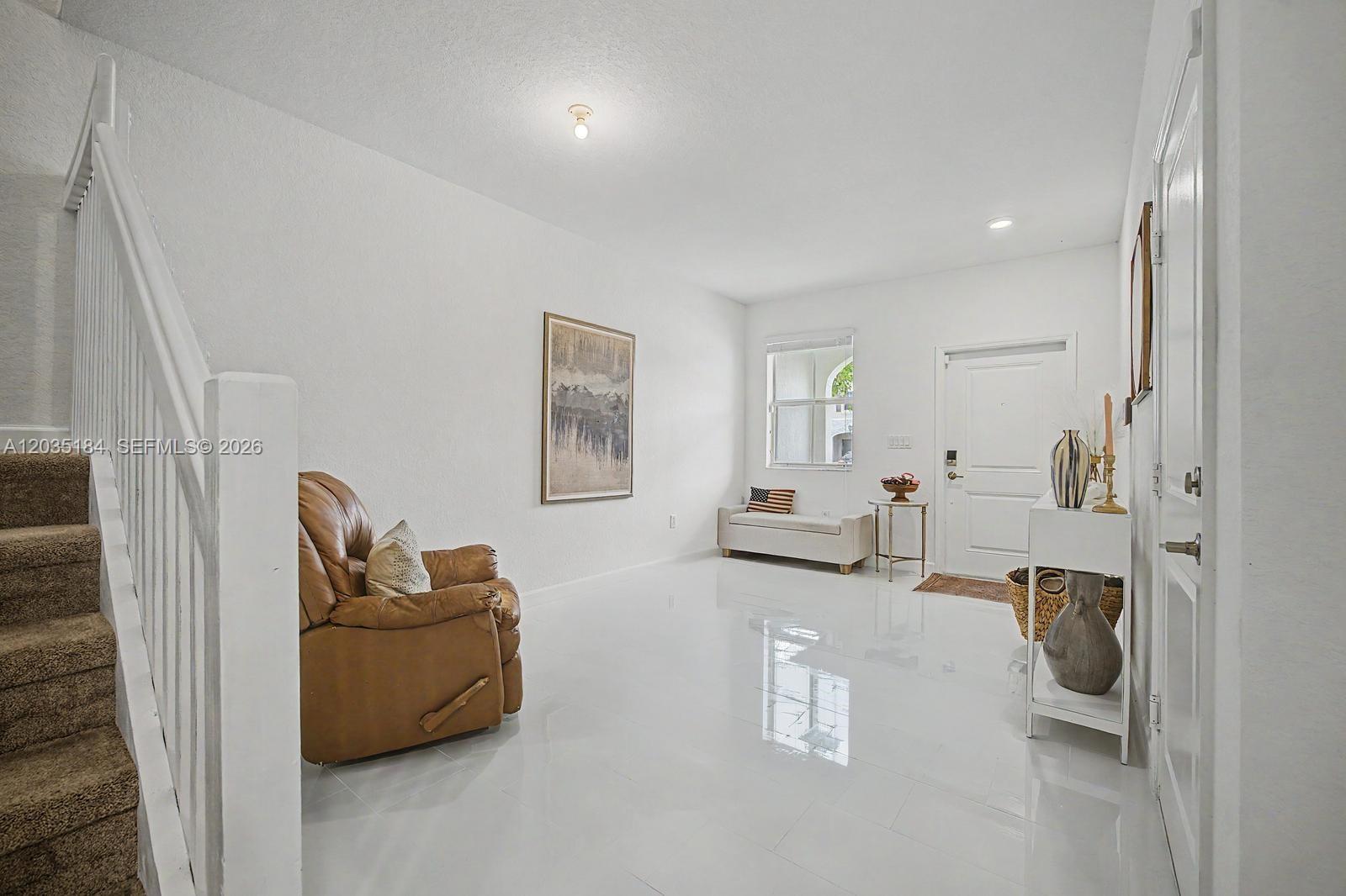 This entryway features white tile floors, a brown leather recliner, and a staircase — 2644 SE 13th St, Homestead FL 33035, HOMESTEAD, FL