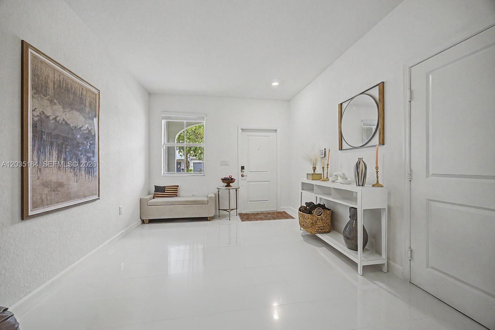 A bright entryway features white tile floors, a console table, a bench, and a front door — 2644 SE 13th St, Homestead FL 33035, HOMESTEAD, FL