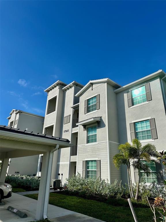 A three-story apartment building with light gray stucco siding and a covered parking area — 17565 OPAL SAND DRIVE UNIT 405, VENICE, FL