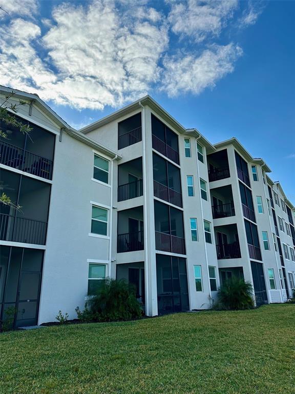 A multi-story apartment building features screened-in balconies and a grassy lawn under a blue sky — 17565 OPAL SAND DRIVE UNIT 405, VENICE, FL