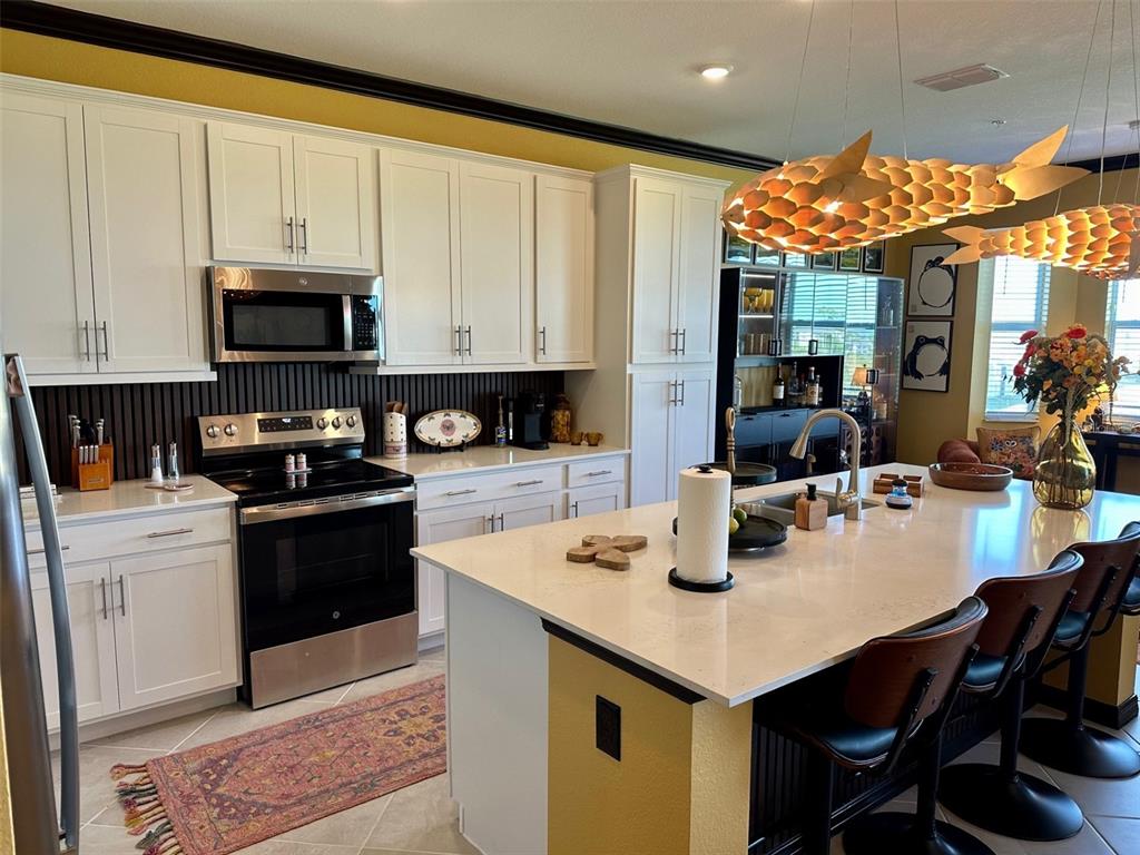 A kitchen features white cabinetry, stainless steel appliances, a large island, and unique pendant lighting — 17565 OPAL SAND DRIVE UNIT 405, VENICE, FL