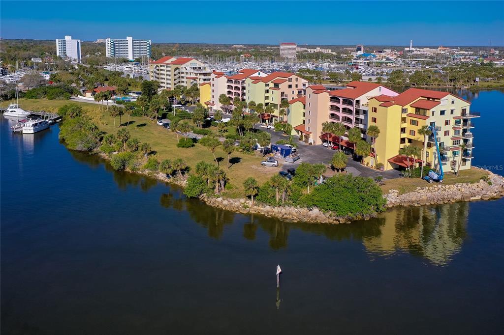 An aerial view shows a multi-story apartment complex situated on a grassy waterfront peninsula — 732 MARINA POINT DRIVE UNIT 7320, DAYTONA BEACH, FL