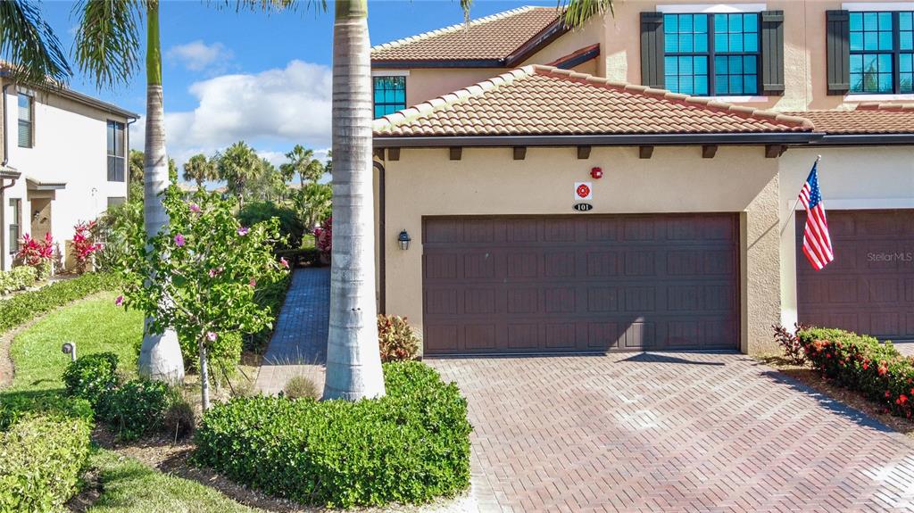 A two-story residential building features a brown garage door, a paved driveway, and palm trees — 10796 TARFLOWER DRIVE UNIT 101, VENICE, FL