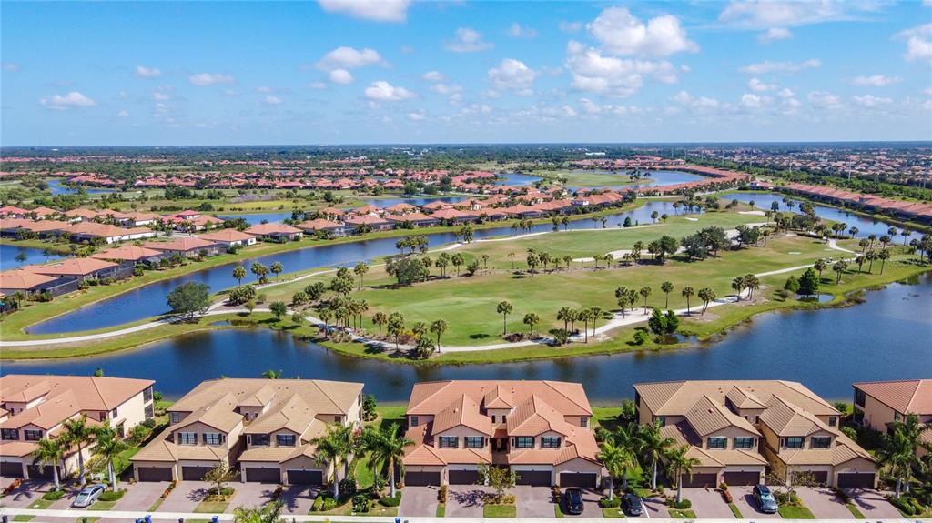 An aerial view shows multi-story townhomes overlooking a golf course and a winding lake — 10796 TARFLOWER DRIVE UNIT 101, VENICE, FL