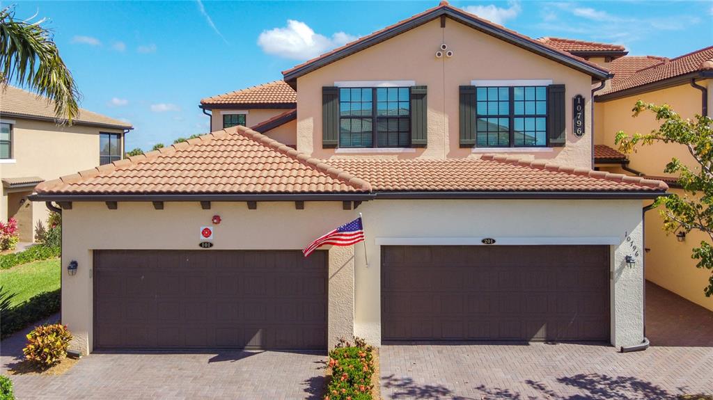 A two-story house exterior features a two-car garage, tan stucco walls, and a tiled roof — 10796 TARFLOWER DRIVE UNIT 101, VENICE, FL