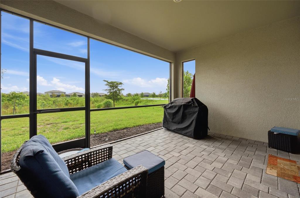 A covered patio with a paver floor, screen enclosure, and a view of a grassy field — 15335 SERENE SHORES LOOP, BRADENTON, FL
