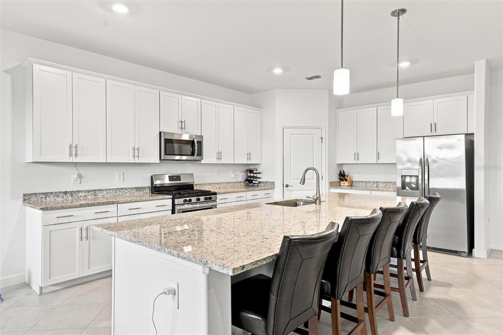 A modern kitchen features white cabinets, granite countertops, a large island, and stainless steel appliances — 15335 SERENE SHORES LOOP, BRADENTON, FL