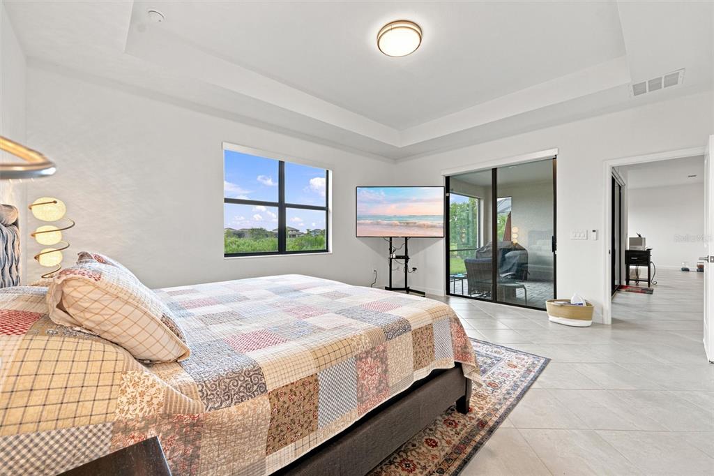 A bedroom with a tray ceiling, tile flooring, a bed, and sliding glass doors to a patio — 15335 SERENE SHORES LOOP, BRADENTON, FL