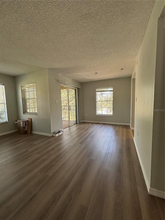 An empty living room features light-colored wood-look flooring, a textured ceiling, and a sliding glass door — 2690 CORAL LANDINGS BOULEVARD UNIT 535, PALM HARBOR, FL